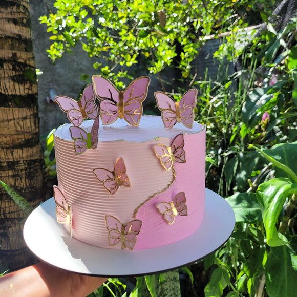 a pink and gold cake with butterflies on the top is being held by a person