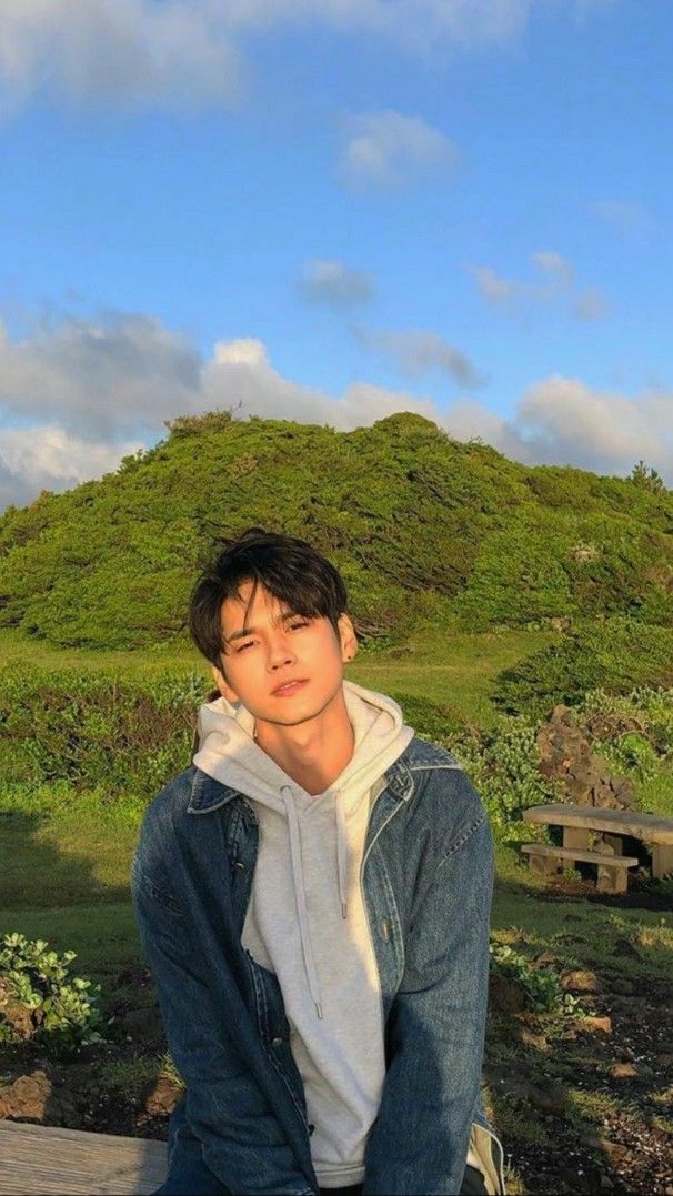 a young man sitting on top of a wooden bench next to a lush green hillside