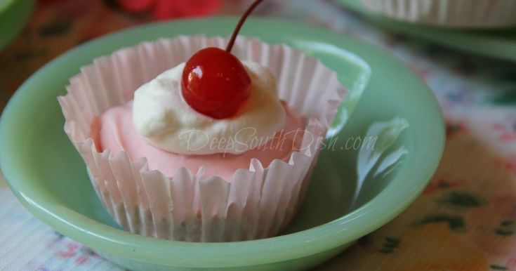 a small cupcake with a cherry on top in a green bowl sitting on a table