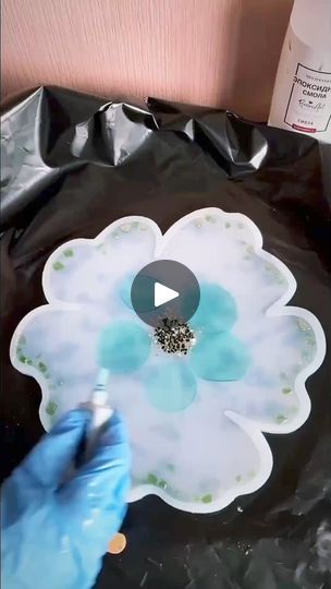 a person in blue gloves is painting a flower on a black bag with white flowers