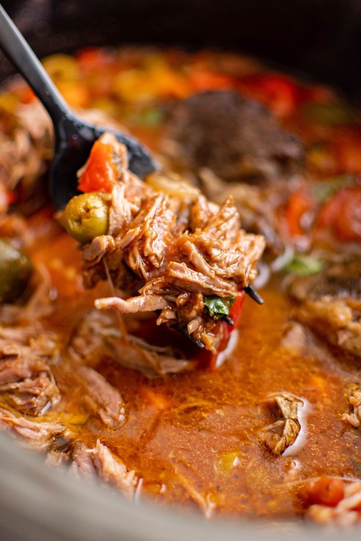 a ladle full of soup with meat and vegetables in it, being held by a spoon