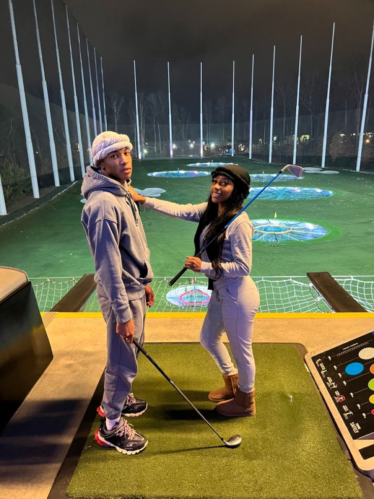 a man and woman standing on top of a green field with golf balls in the air