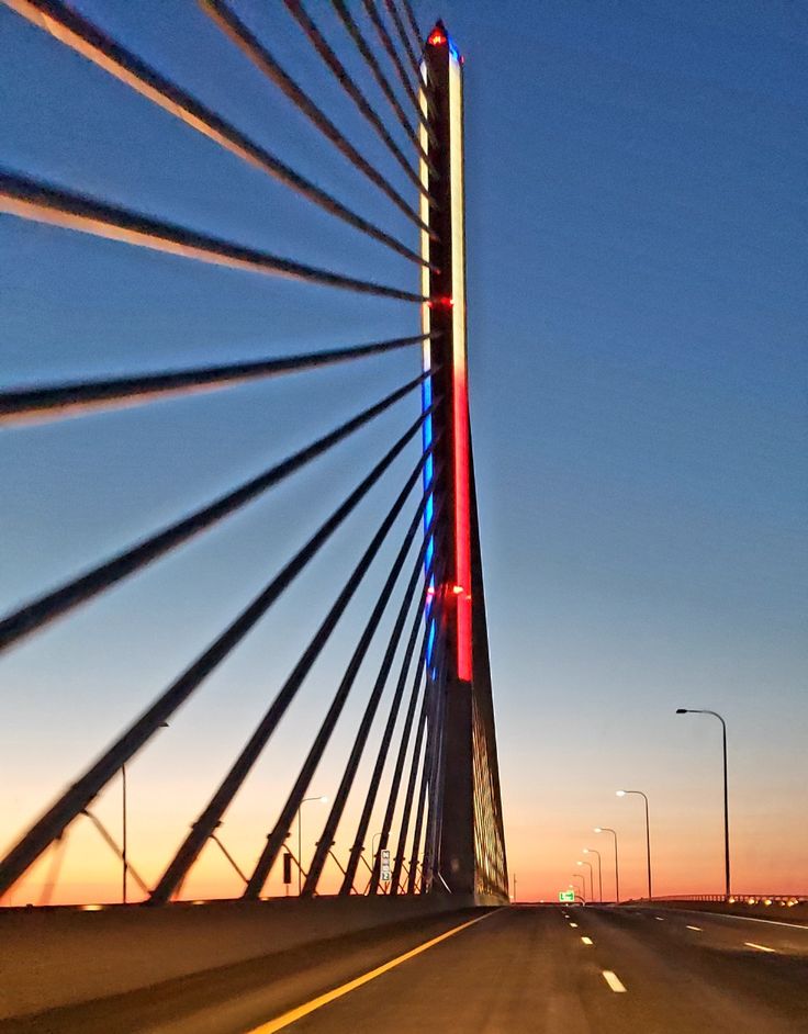 the sun is setting behind a very tall bridge that has many lights on it's sides