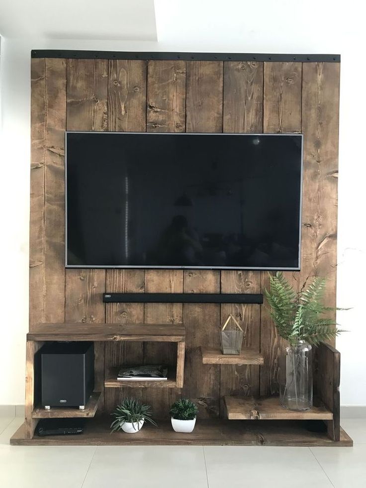 a flat screen tv mounted to the side of a wooden wall next to potted plants