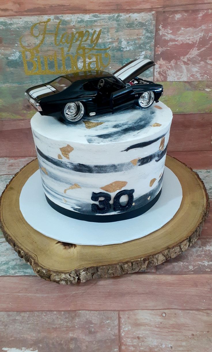 a white cake with a black car on top and happy birthday written in gold lettering