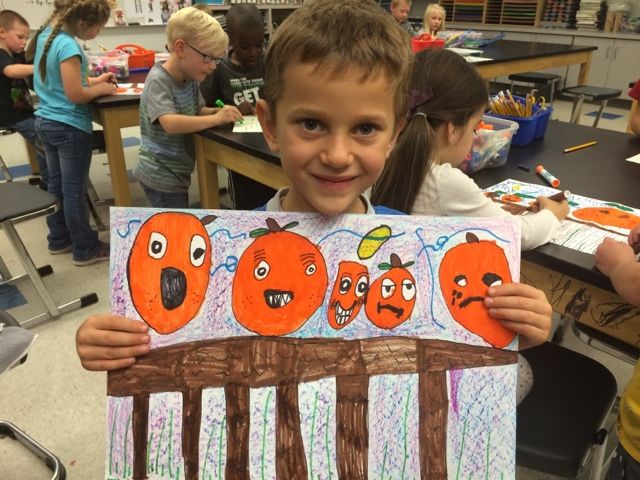 a young boy holding up a drawing with oranges on it