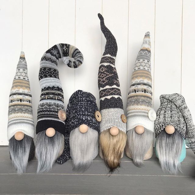 several knitted gnomes are lined up against a white wall and one is laying on the floor