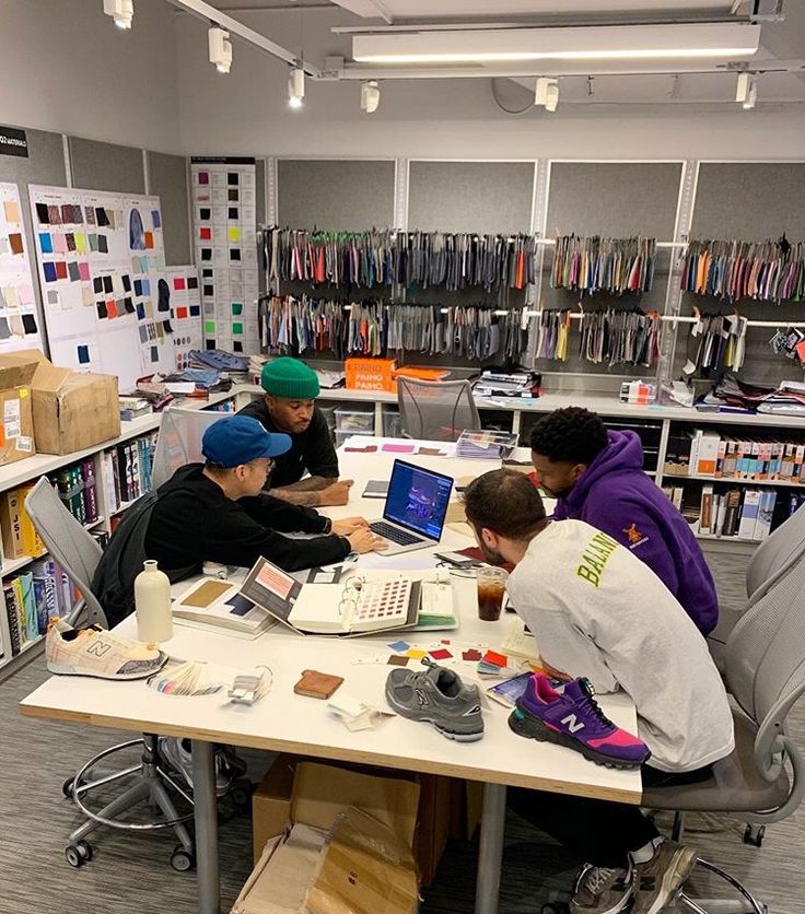 three boys sitting at a table working on their laptops in the middle of a library