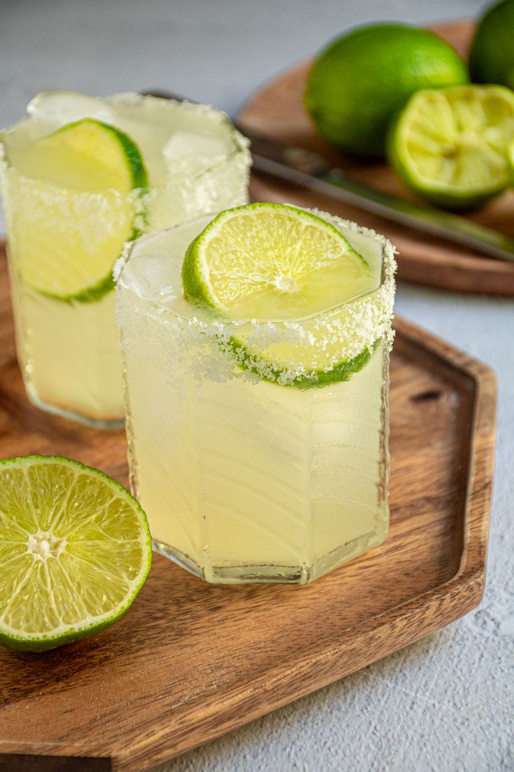 two lime margaritas on a wooden cutting board