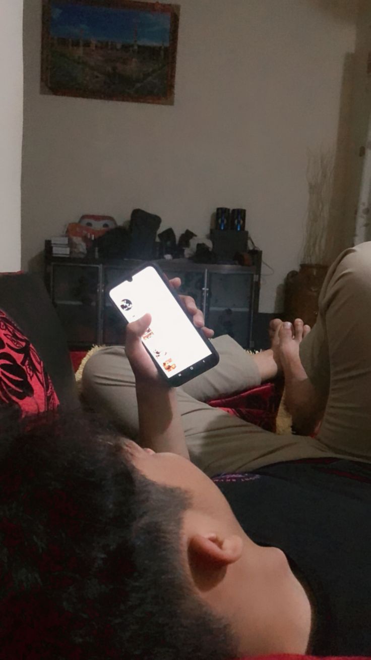 a person laying on a couch with a cell phone in their hand while another person lays down next to them