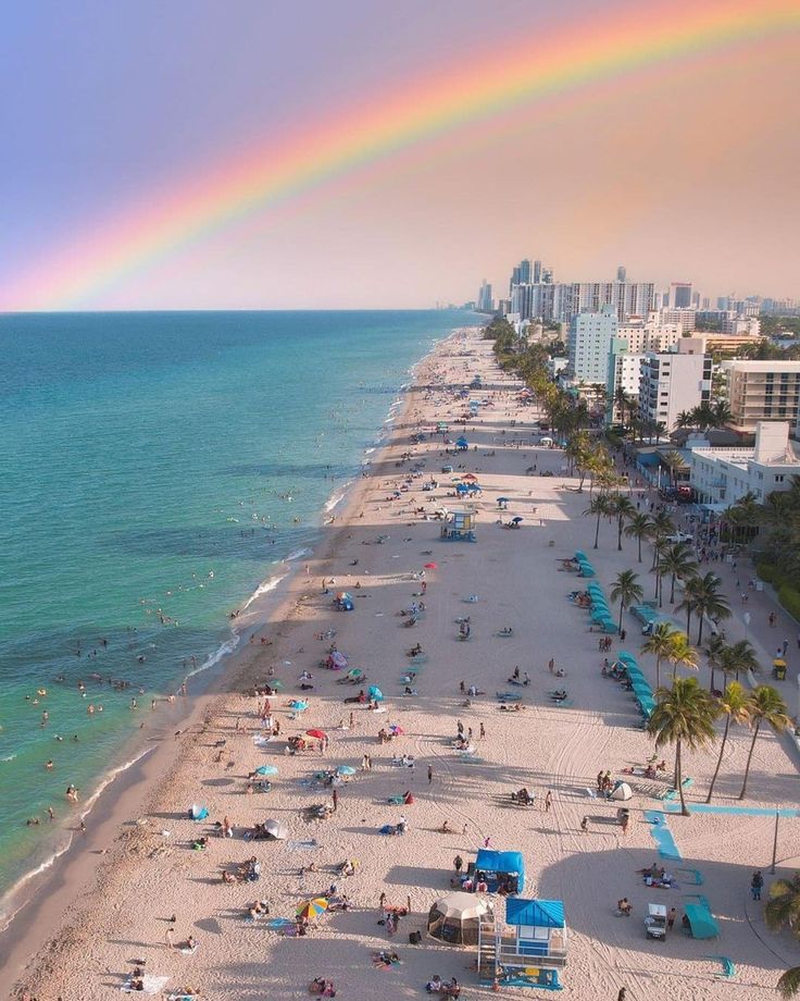 a rainbow is seen over the beach as people sunbathe and swim in the water