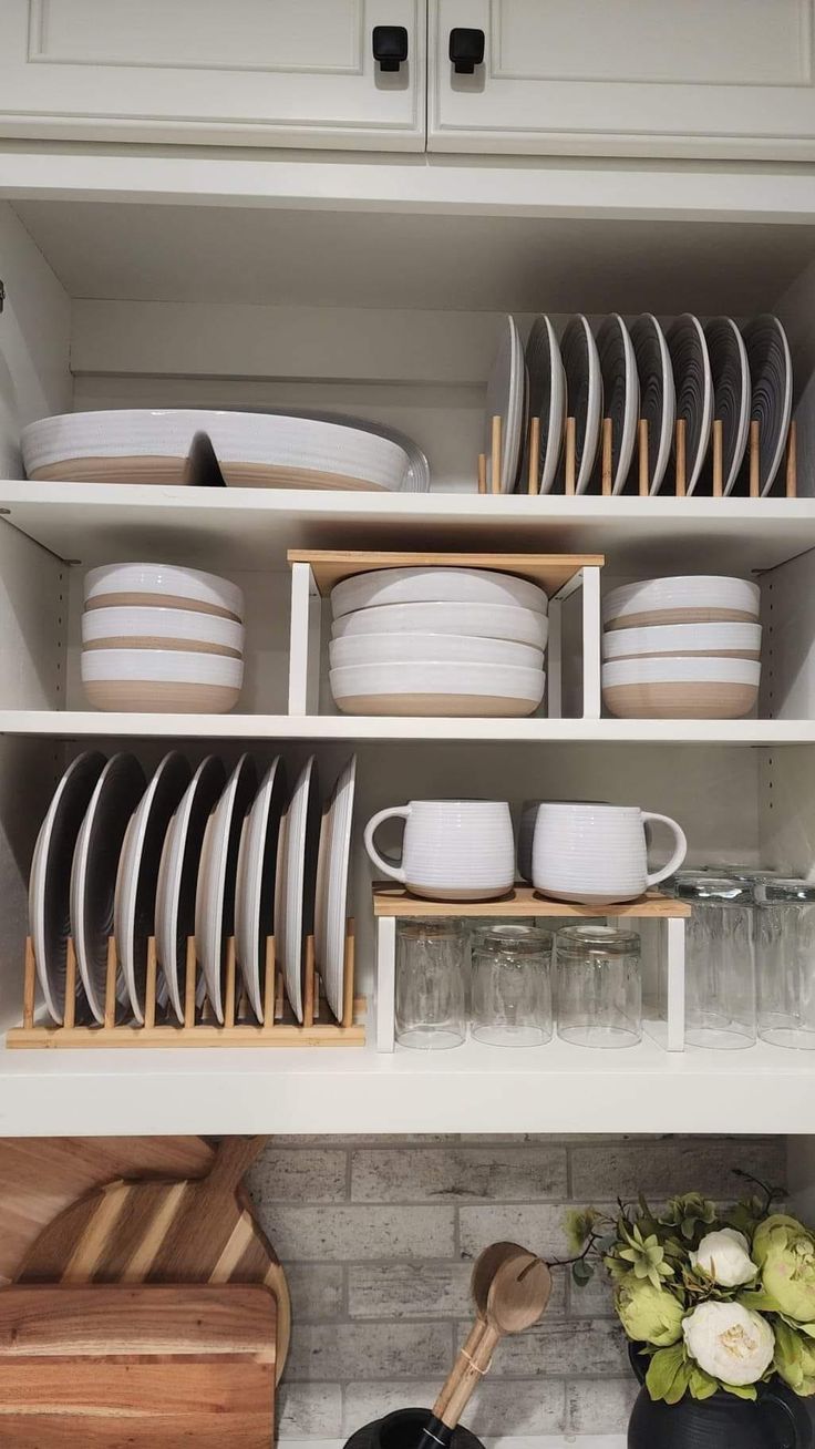 white dishes and wooden utensils are stacked on the shelves in this clean kitchen