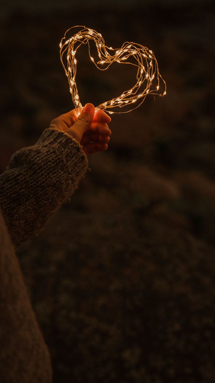 a person holding a heart shaped string in their hand with the light shining through it