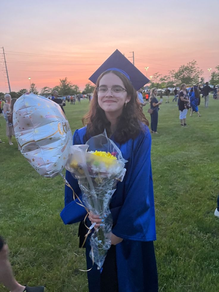 a woman in graduation gown holding flowers and balloons at the end of her graduation day