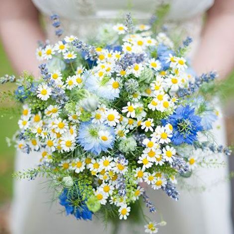 a bouquet of daisies and other flowers in a woman's hand with the background blurry