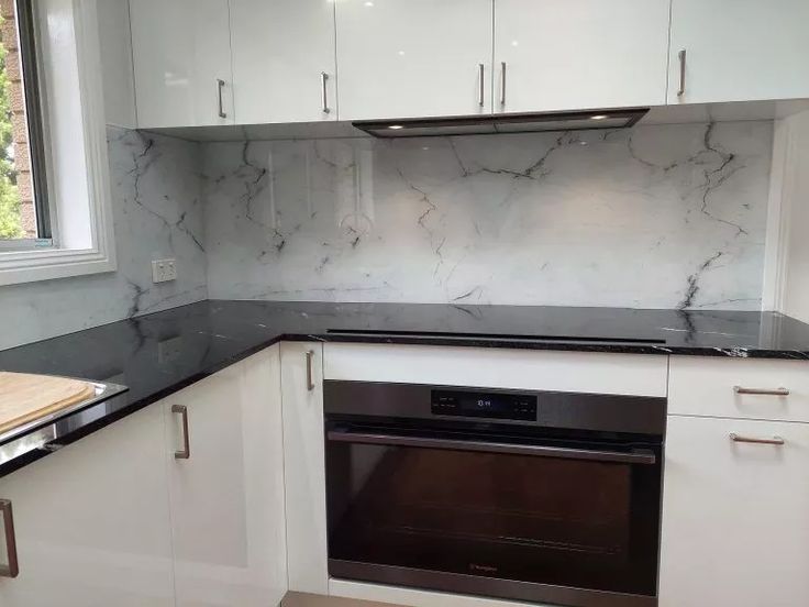 an empty kitchen with white cabinets and black counter tops is pictured in this image, there is a wooden cutting board on the counter