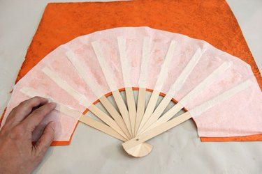 a hand holding a wooden fan on top of an orange and white cloth covered table