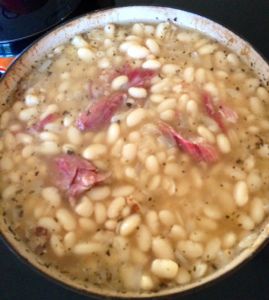 a pot filled with beans and ham sitting on top of a stove next to a can of soda