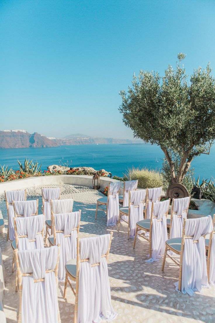 an outdoor wedding setup with white linens and chairs overlooking the ocean in front of some olive trees