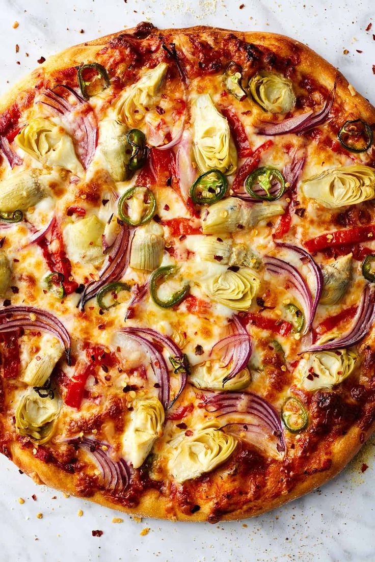 a pizza topped with onions, artichokes and other toppings on a white surface