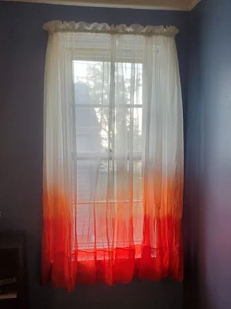 an orange and white ombreed curtain hangs in front of a window with blue walls