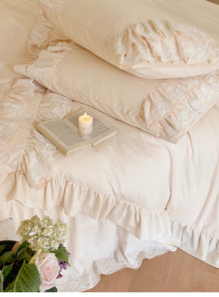 a stack of pillows sitting on top of a bed next to a vase with flowers