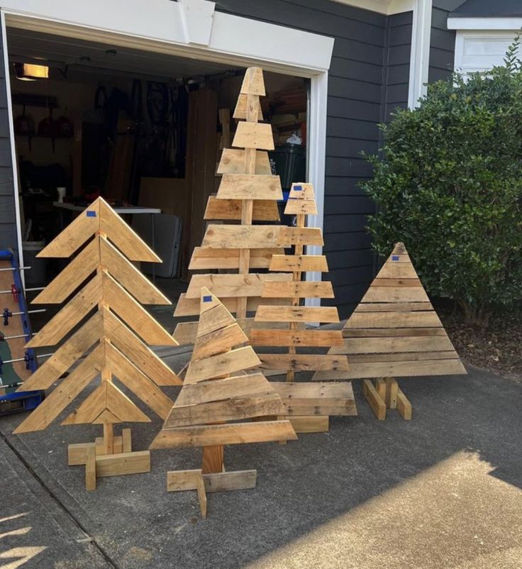 several wooden christmas trees sitting on the ground in front of a garage with one being made out of wood planks