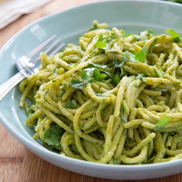 a bowl filled with green pasta on top of a wooden table