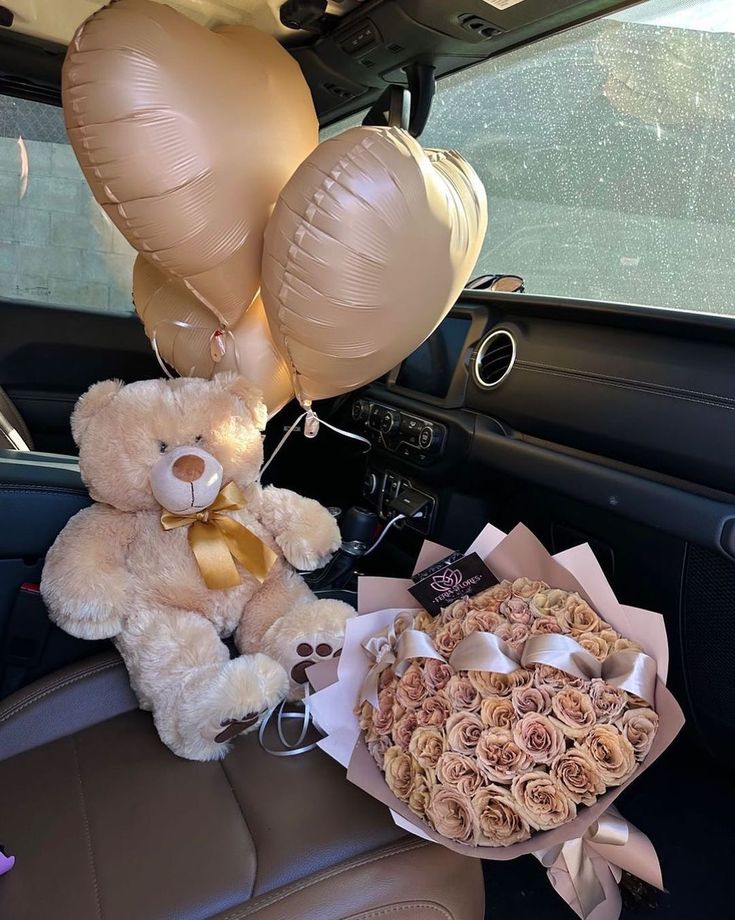 a teddy bear sitting in the back seat of a car next to balloons and flowers