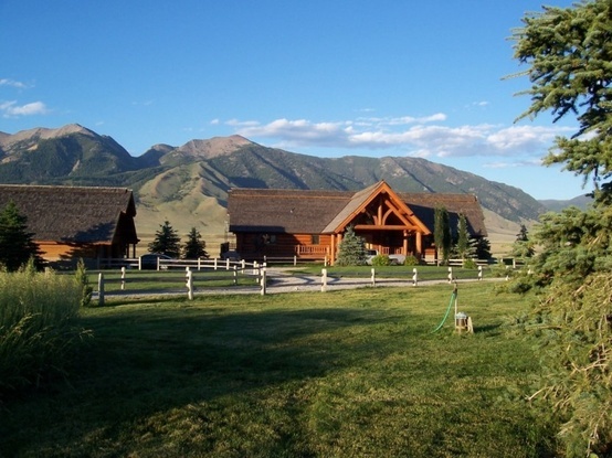 a large wooden house sitting in the middle of a lush green field next to mountains