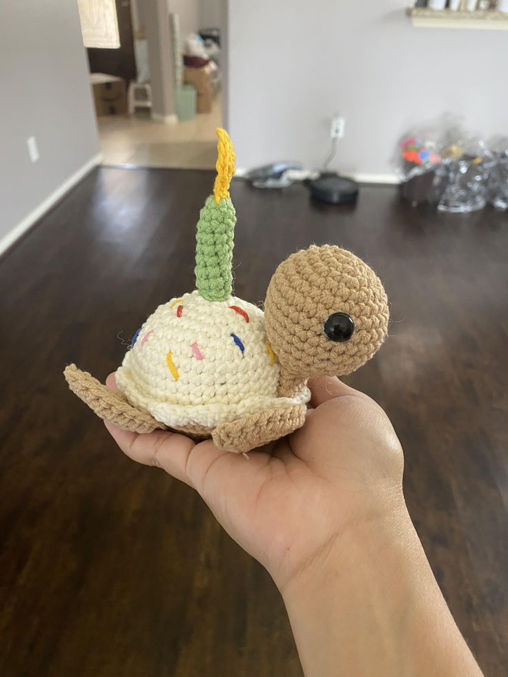 a hand holding a small crocheted snail with a birthday hat on it's head