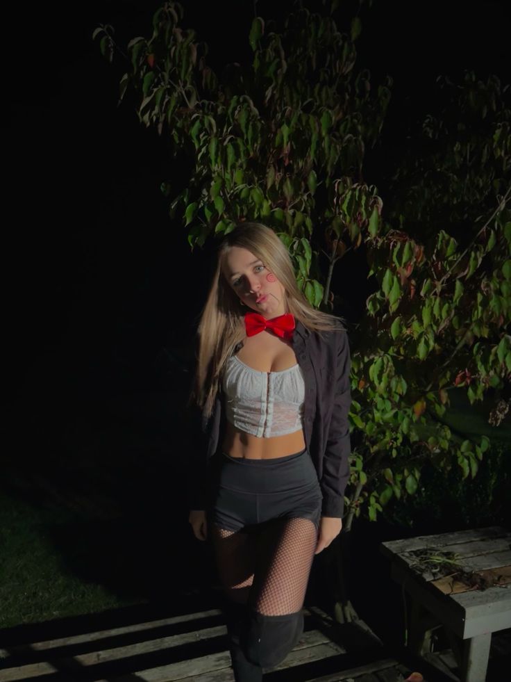 a woman in short shorts and a red bow tie posing on a bench at night