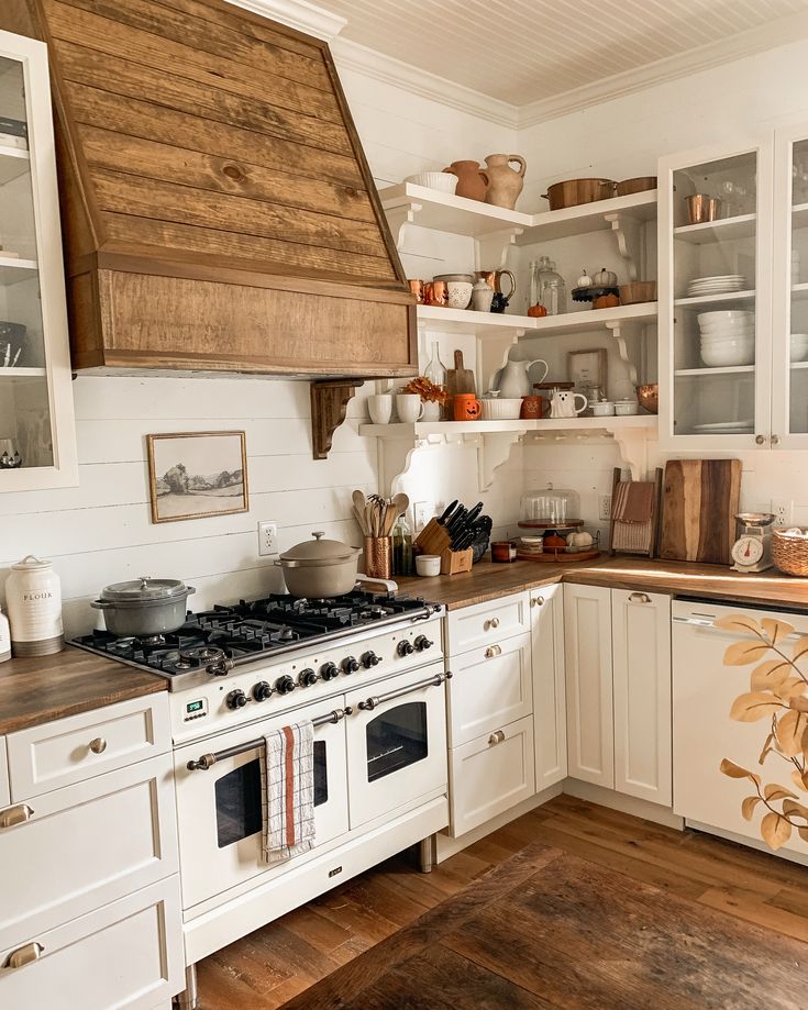 a kitchen with white cabinets and wood flooring has an open range hood over the stove