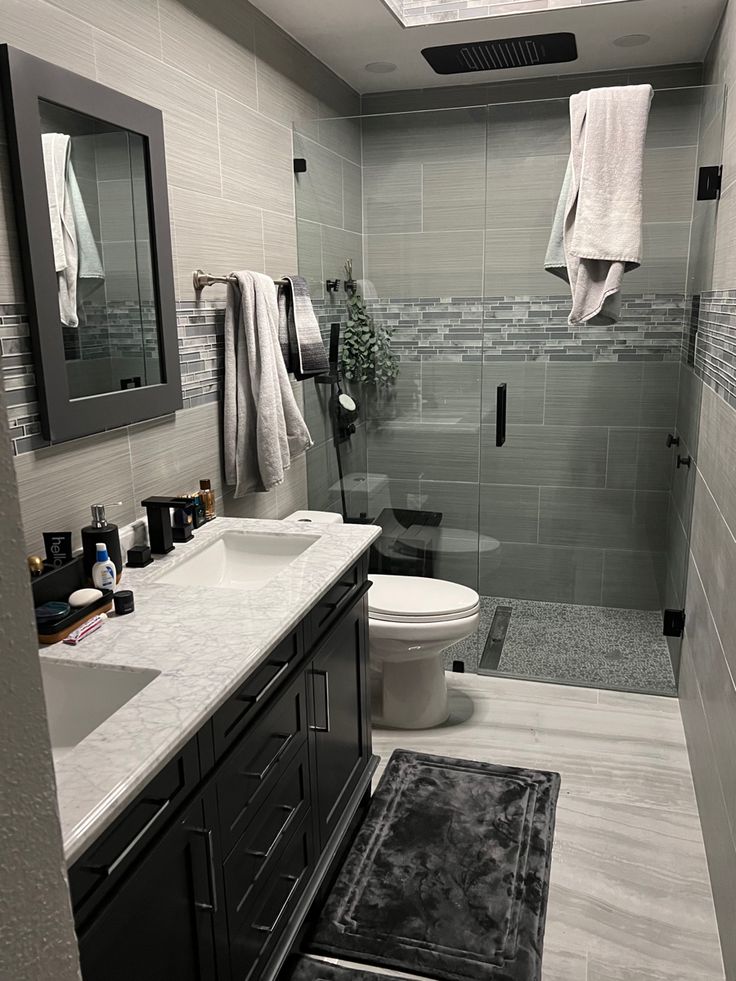 a bathroom with a glass shower door and white counter tops, black cabinetry, gray tile floor