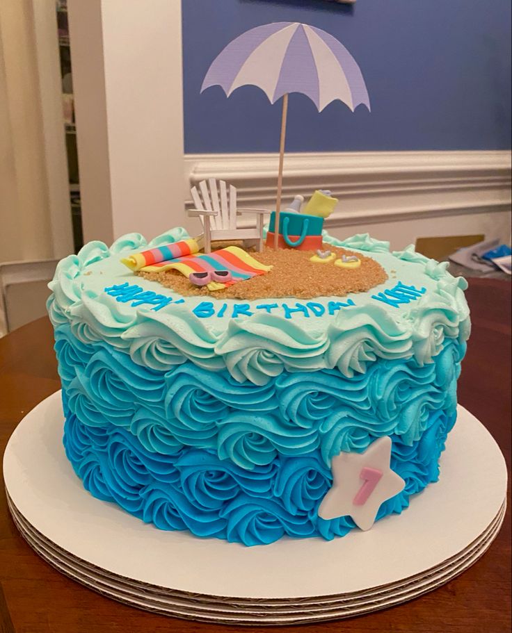 a birthday cake decorated with blue icing and an umbrella on the top is sitting on a table