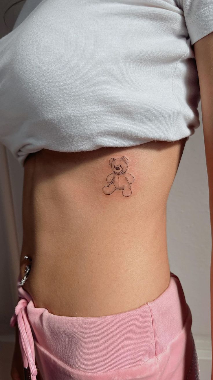 a woman with a teddy bear tattoo on her lower side ribcage, showing it's stomach