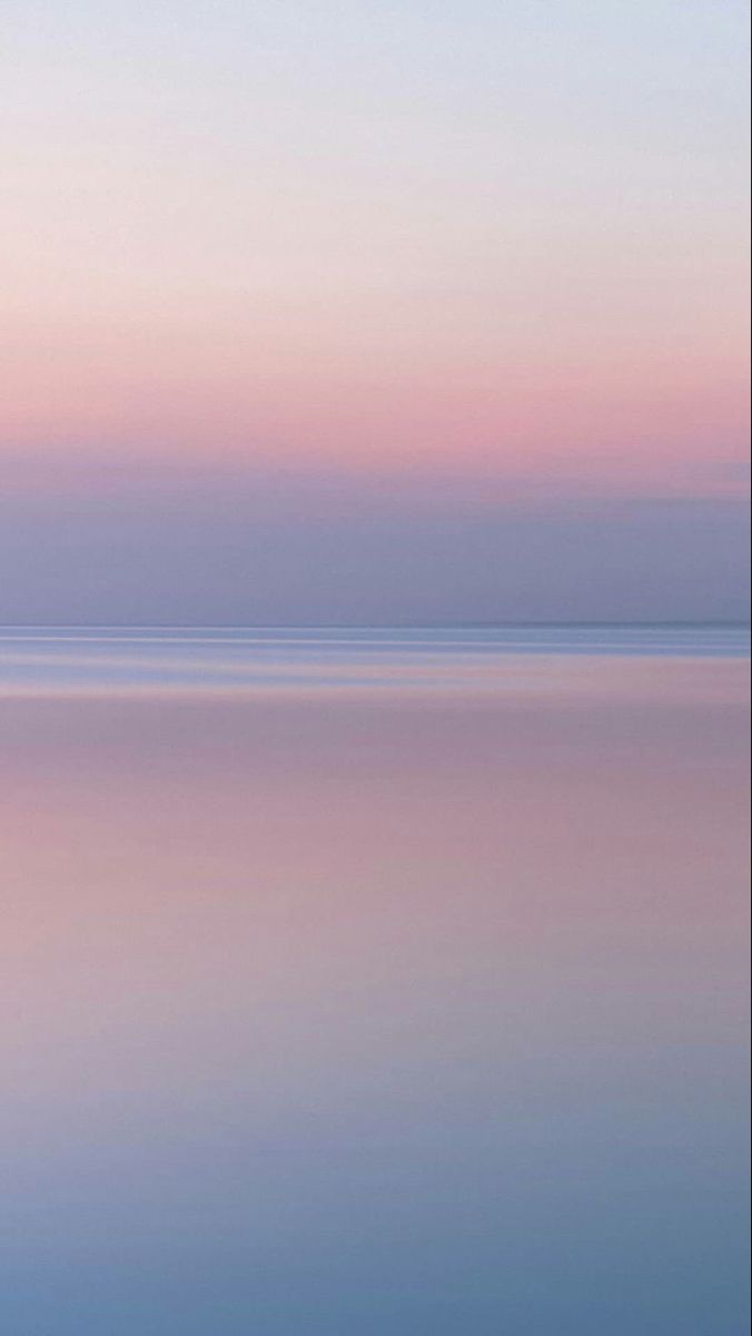 a lone boat floating on top of a large body of water under a pink sky