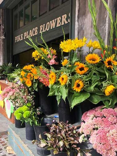 many different types of flowers are on display in front of a flower shop, including sunflowers and daisies