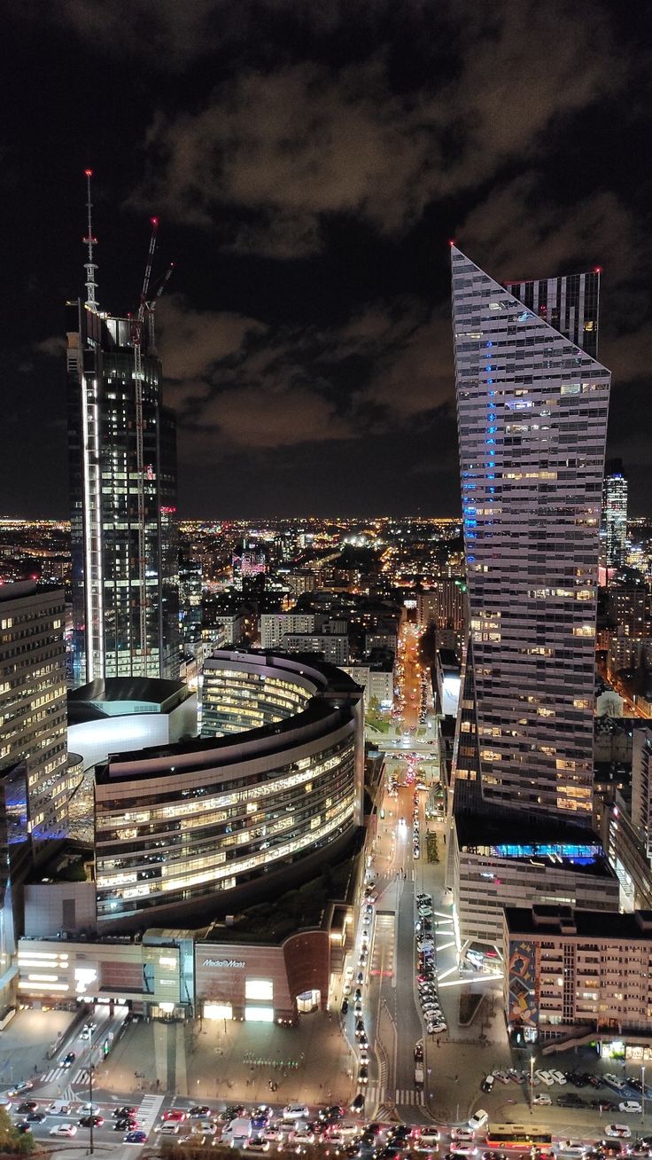 an aerial view of a city at night with tall buildings in the foreground and cars on the street below