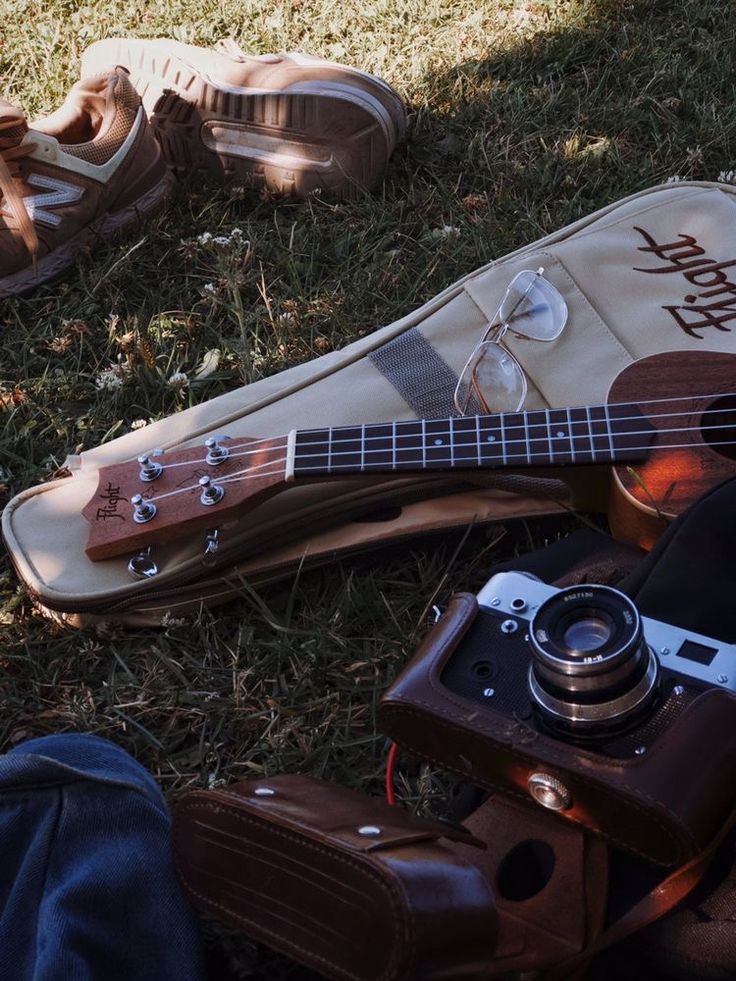 a guitar, camera and shoes laying on the ground in the grass near someone's feet