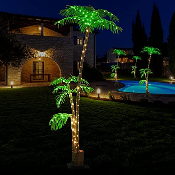 lighted palm trees in front of a house at night with swimming pool and patio area