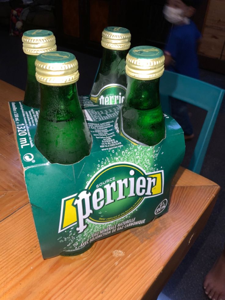 three bottles of perrier sitting on top of a wooden table next to a person