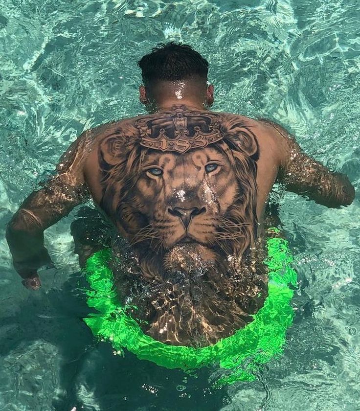 a man with a lion tattoo on his back swimming in the water while wearing a green ring around his neck