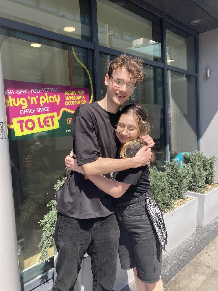 a man and woman standing in front of a store with their arms around each other