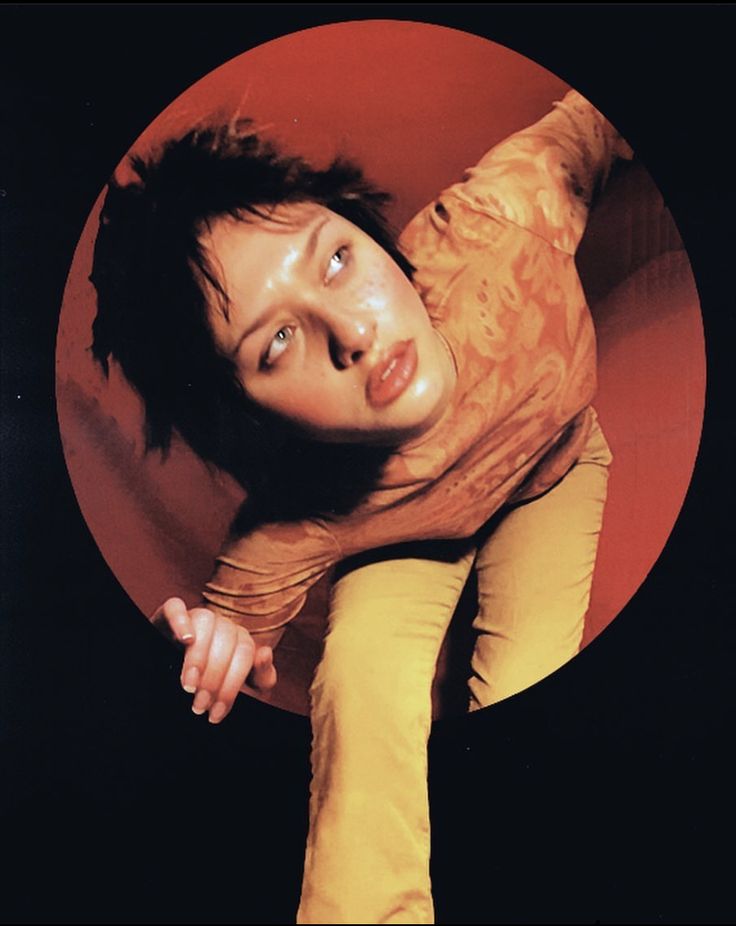 a woman is laying down in front of a red and black circular object with her head tilted to the side