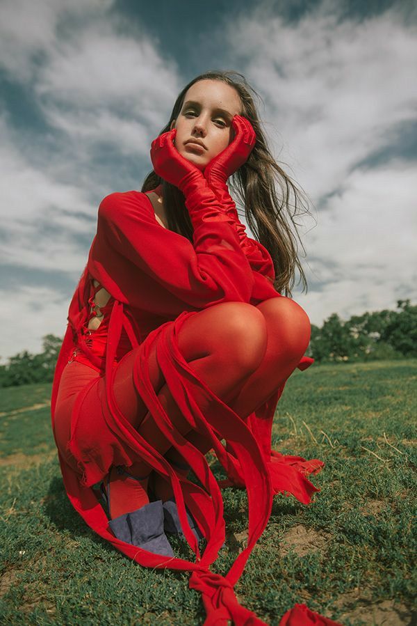 a woman in a red dress sitting on the ground with her hands behind her head