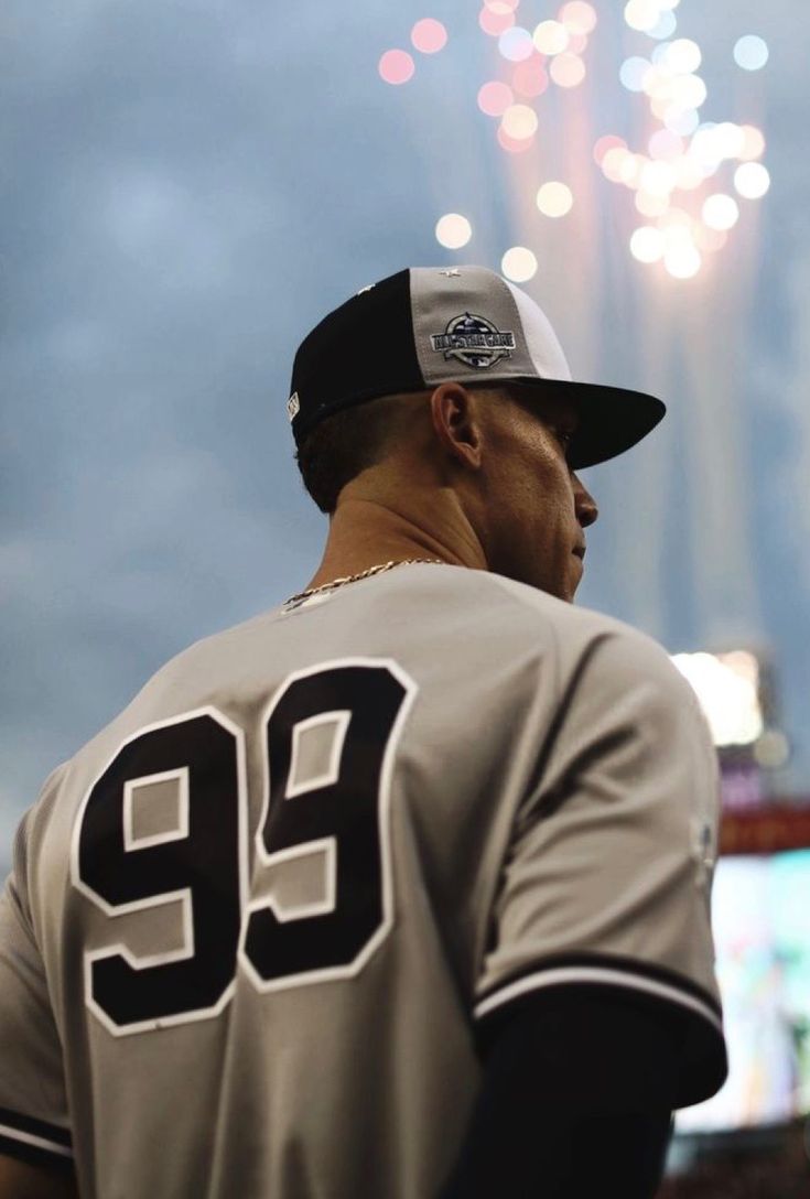 a baseball player wearing a gray and black uniform with fireworks in the sky behind him