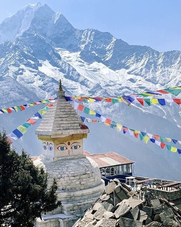 there is a small building on top of the mountain with flags flying in the wind