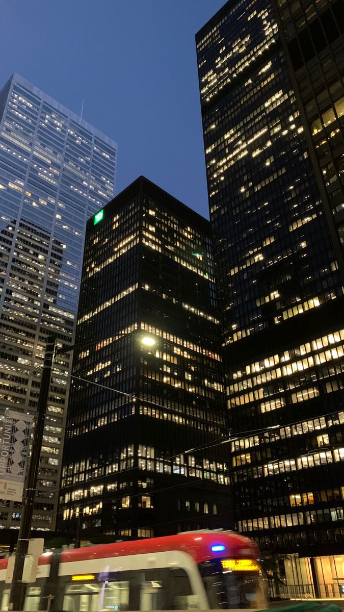 a bus driving past tall buildings in the city at night with green lights on them