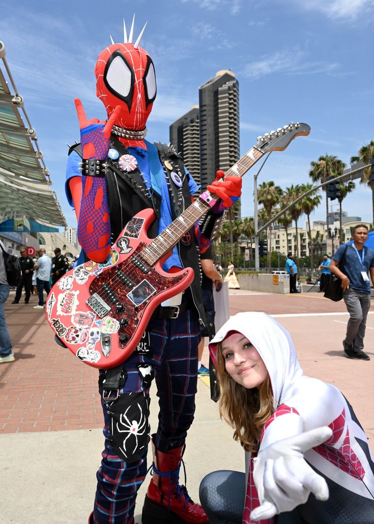 two people dressed up as deadpool and spider - man, one holding a guitar